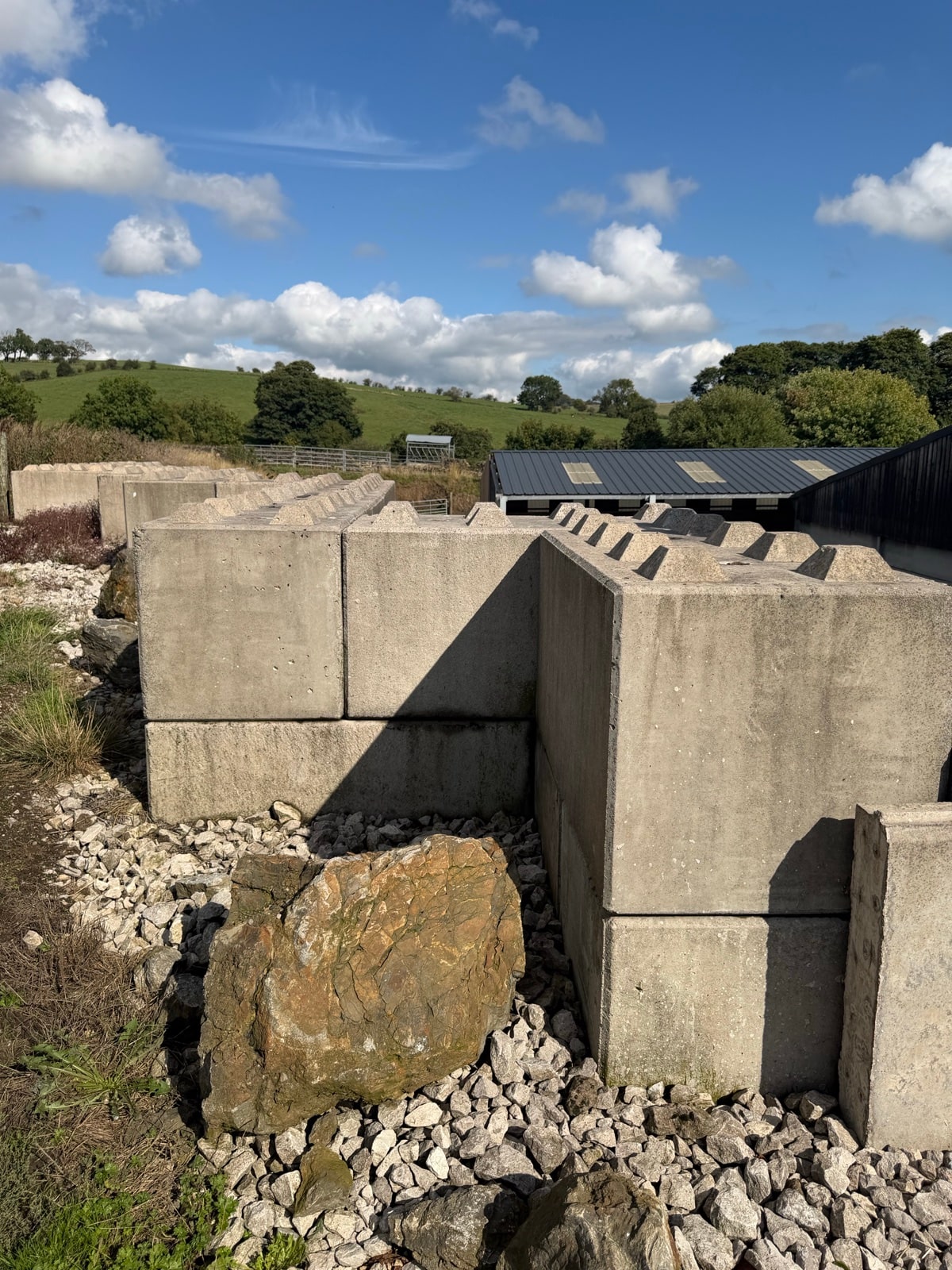 Giant interlocking concrete blocks stacked beside farm buildings, resembling oversized Lego bricks