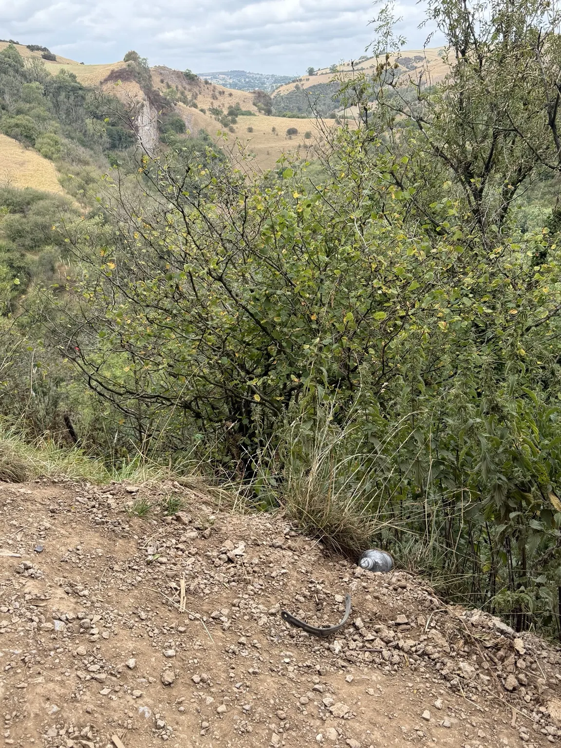 A broken Crocs strap and an abandoned plastic bottle beside the path above the Manifold Valley